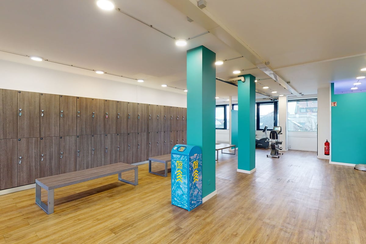 PureGym Dietikon: Wooden lockers, bench, teal accents, rubberized flooring in a gym changing area.
