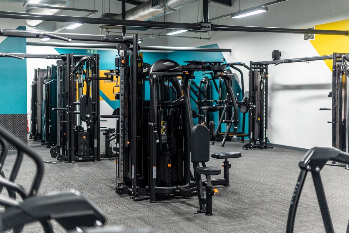 PureGym Ashton Under Lyne: Rows of weight machines, cable stations, and free weight racks in a gym studio with teal walls.