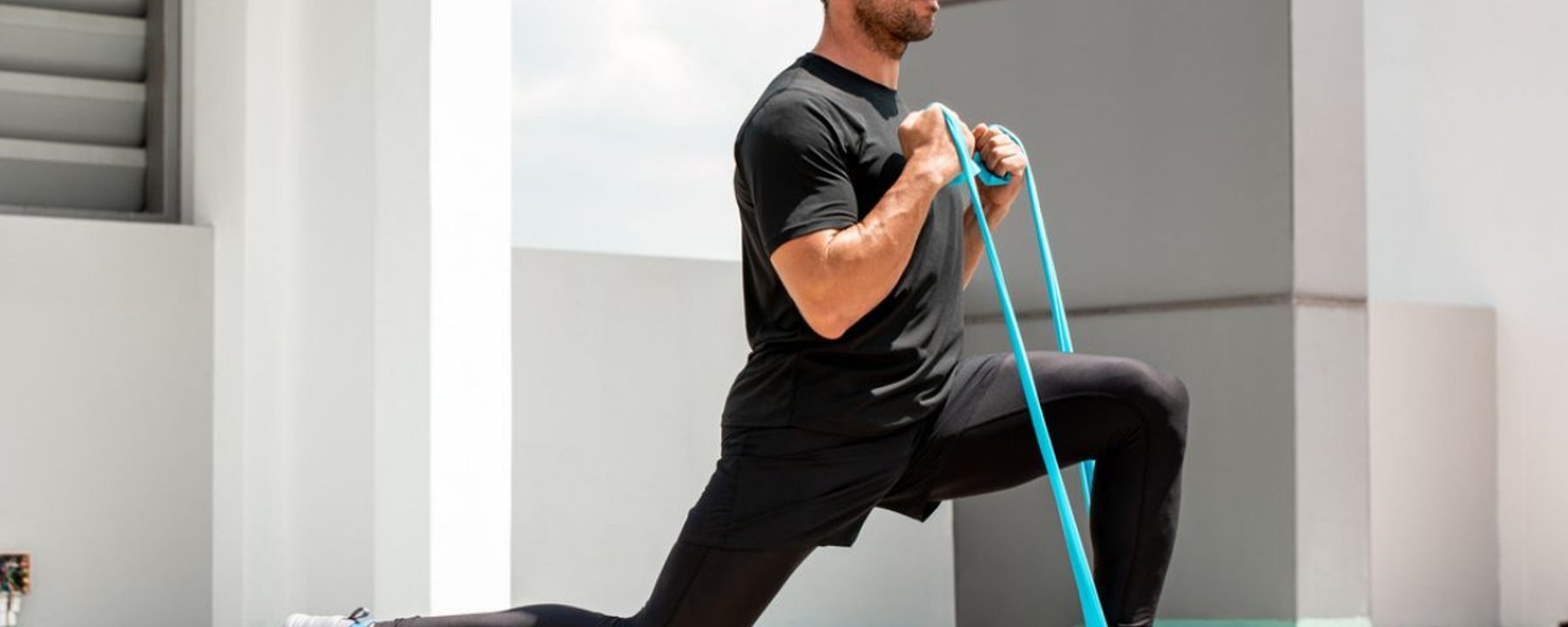 Homme en tenue de sport noire s'exerçant avec une bande de résistance sur un toit