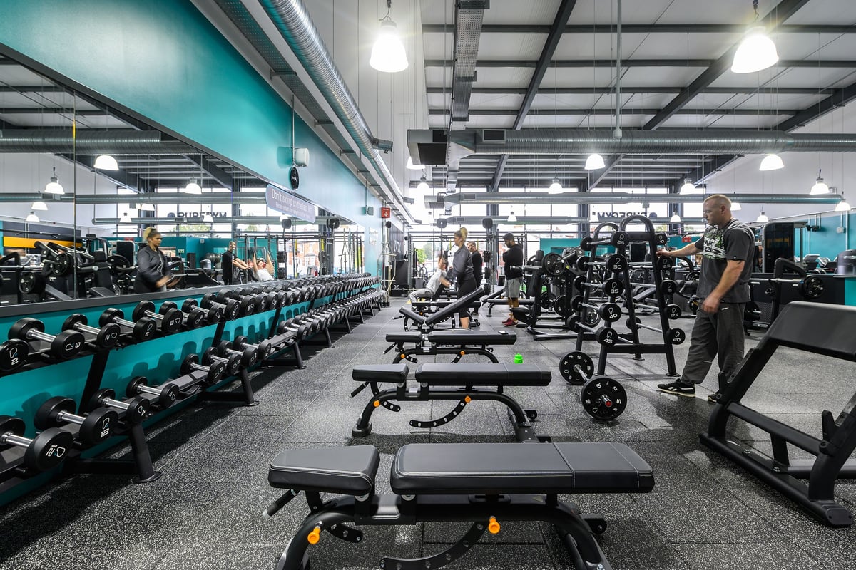 PureGym Bromsgrove Retail Park: Rows of weight benches, dumbbells, and weight racks on rubberized gym flooring.