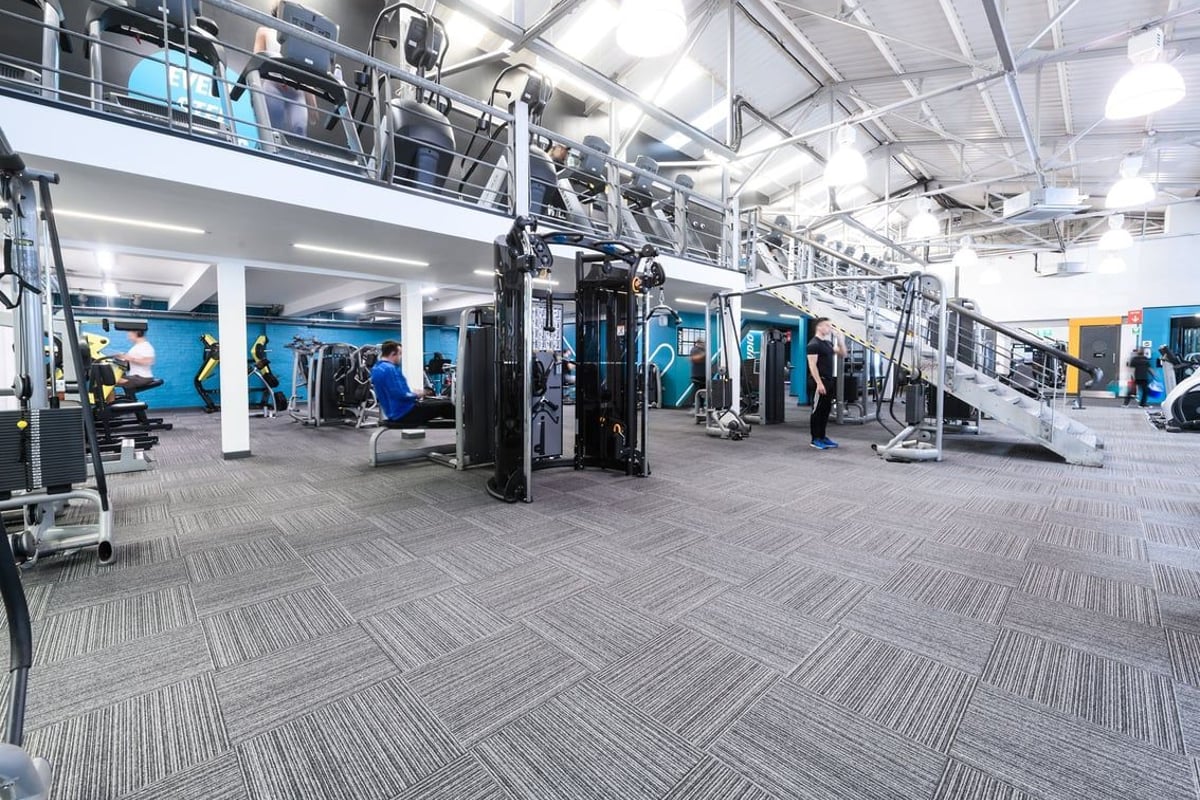 PureGym London Clapham: Gym studio with weight machines, free weights, rubberized flooring, and vibrant blue accent walls.