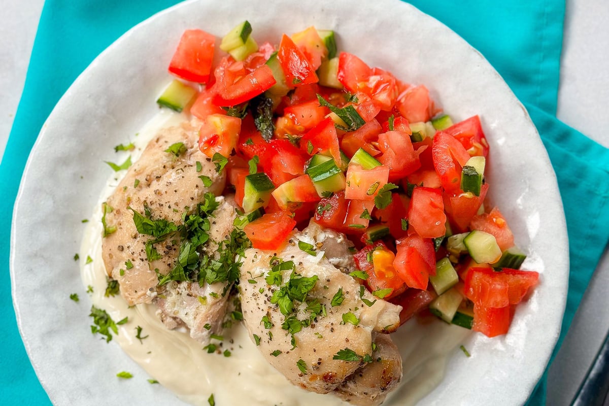 Grilled chicken thighs with chopped tomato and cucumber salad on white sauce on a plate