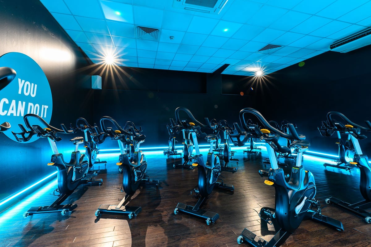 PureGym Mansfield: Rows of stationary cycles in a dimly lit studio with motivational wall art and blue neon lighting.