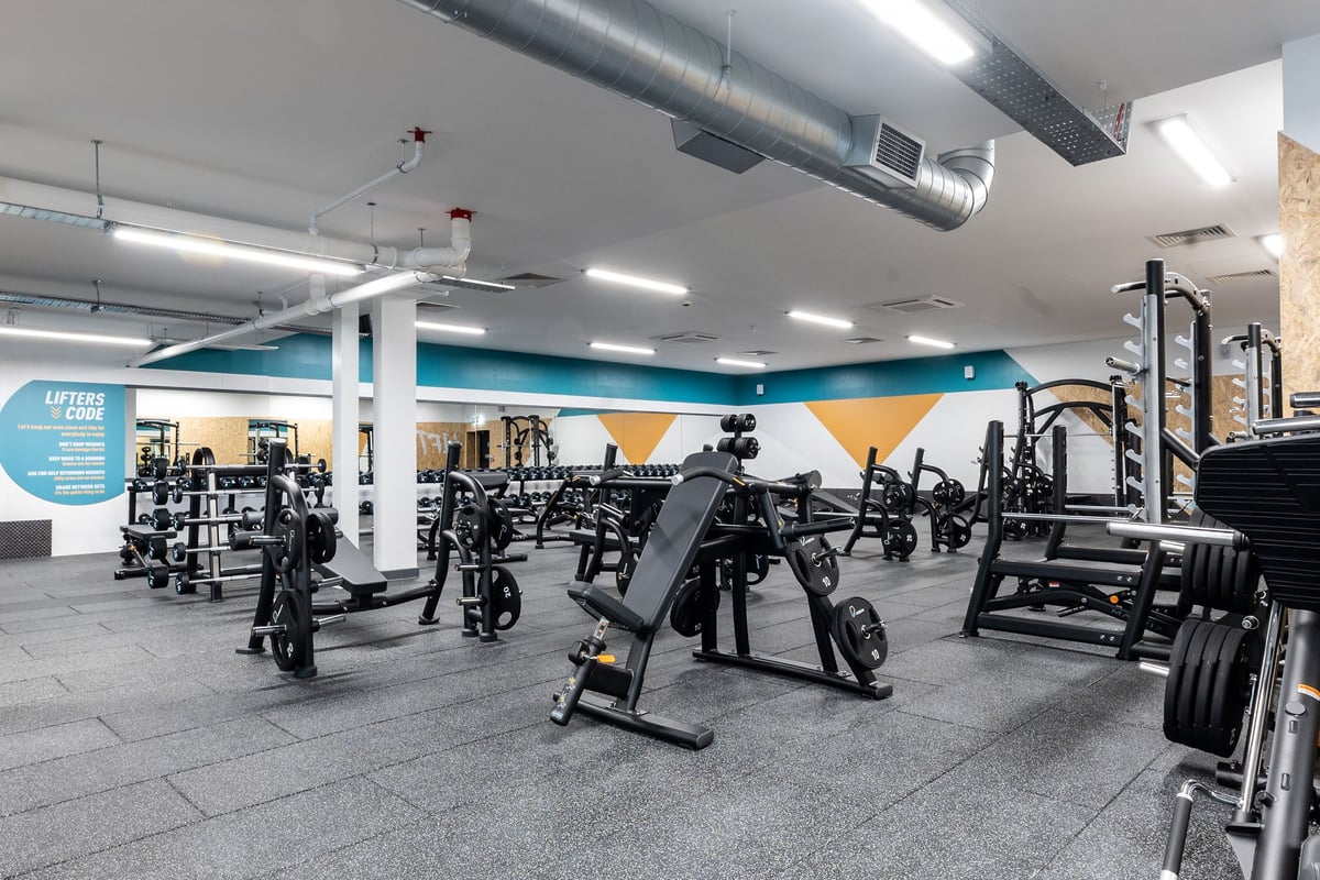 PureGym Glasgow Giffnock: Gym interior with weight machines, free weights, benches, mirrors, and patterned rubber flooring.