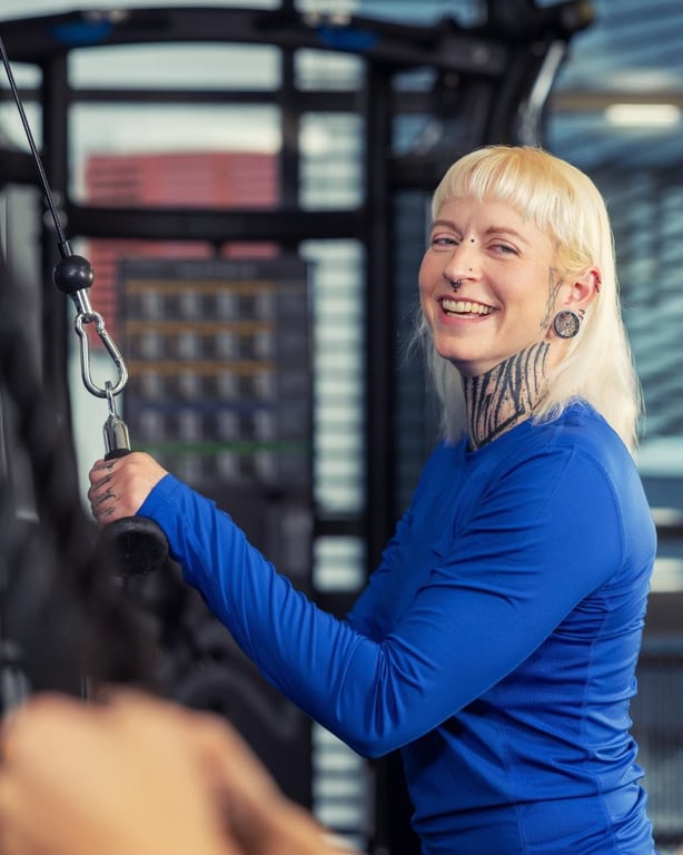 Smiling woman in blue workout gear using cable machine in modern gym with equipment visible in background