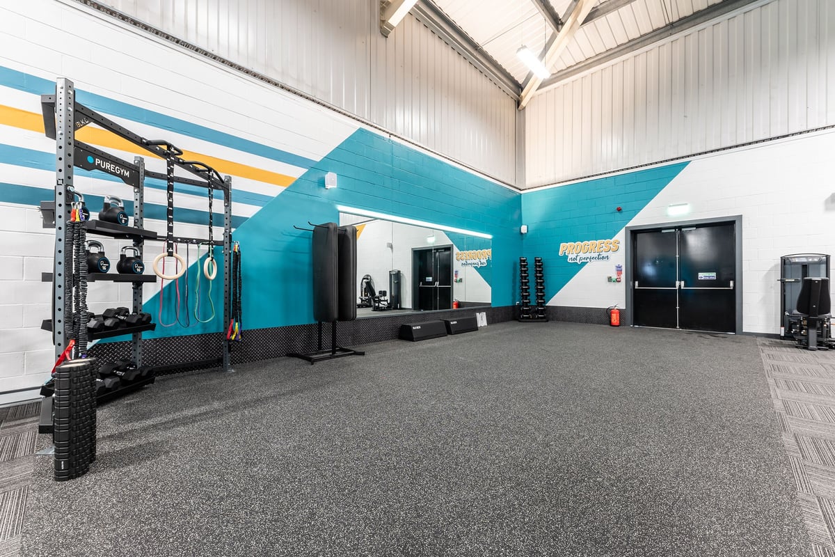 PureGym Merthyr Tydfil: Large grey floor area with resistance machines, turf track, colourful accent walls.