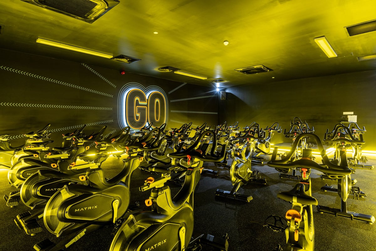 PureGym Loughborough: Rows of stationary bikes in a dimly lit studio with neon 'GO' signage.