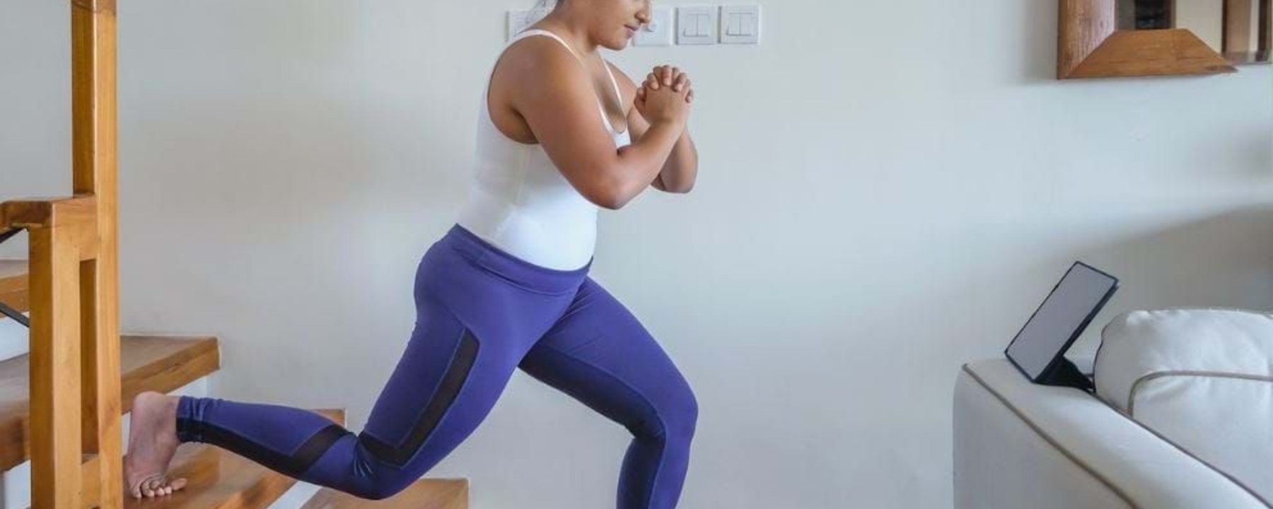 Woman exercising with one foot on stairs and the other on the floor indoors