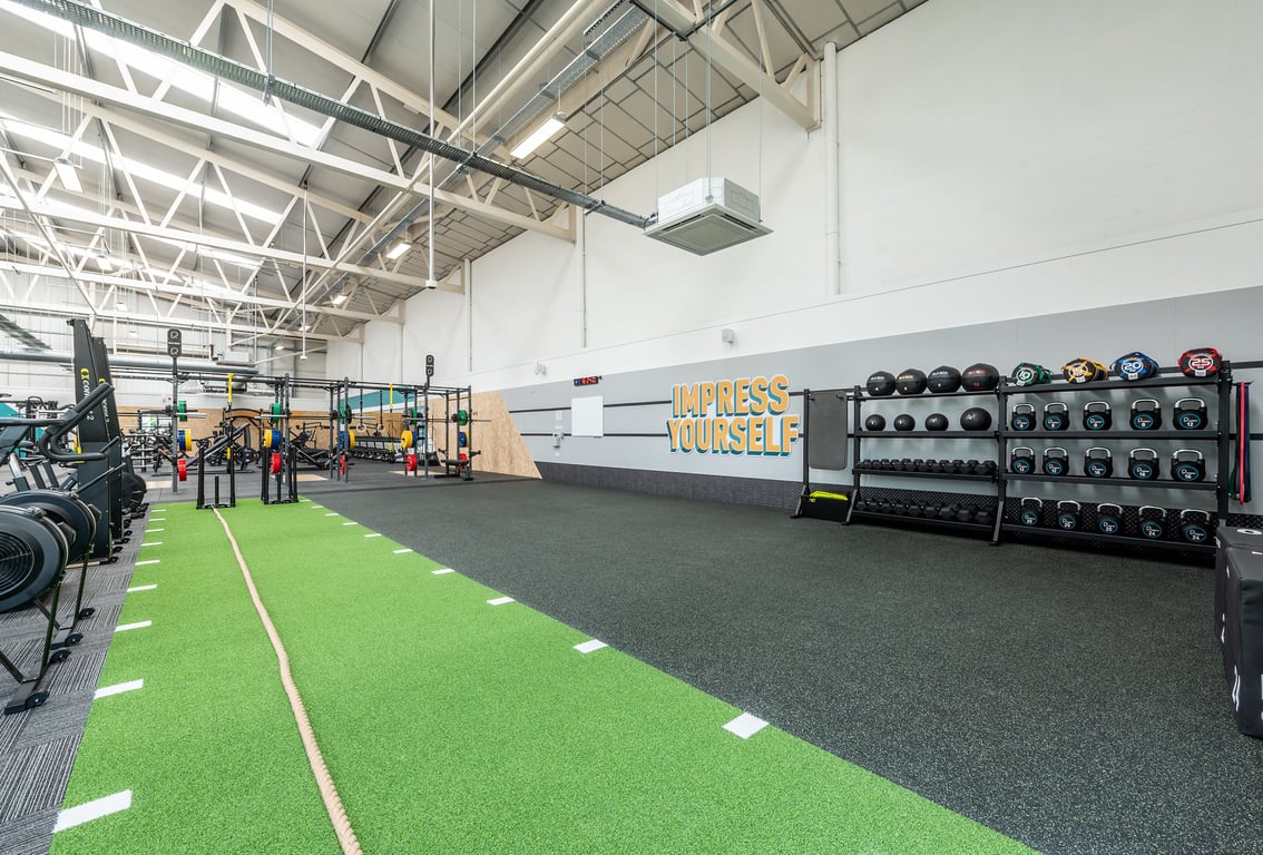 PureGym Bridgend: Weights racks, free weights, rubberized flooring, artificial turf area, ceiling-mounted fans.