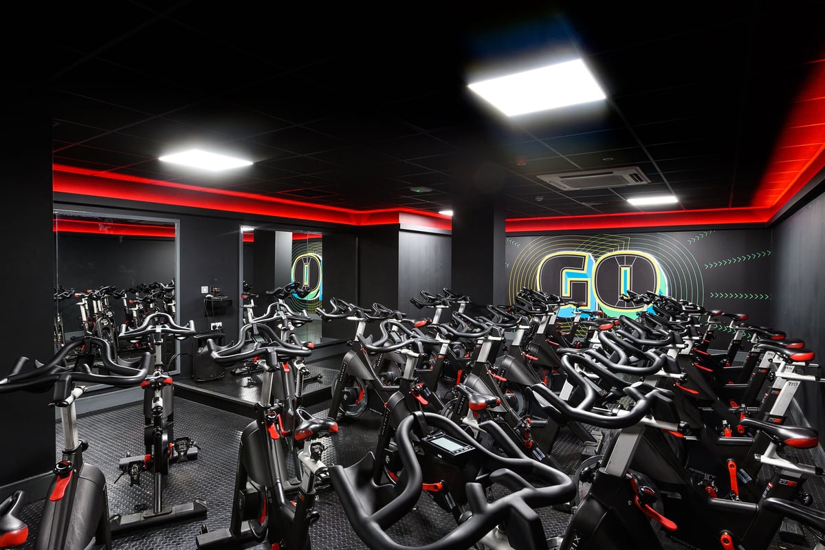 PureGym Oxford Central: Rows of stationary cycles with red accents and bright lighting in a cycling studio.