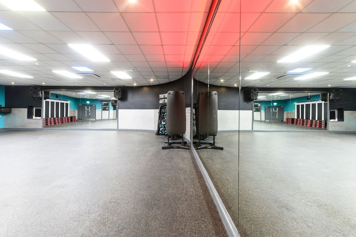 PureGym Waterlooville: Mirrored walls, punching bags, red lighting, padded floors - a boxing or martial arts studio.