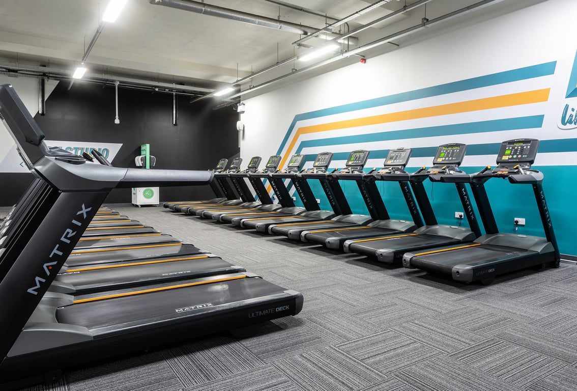 PureGym London Bermondsey: Row of modern treadmills in a gym studio with teal accents along the walls.