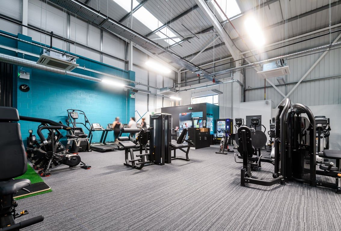 PureGym Buckingham: Weight training equipment, resistance machines, benches, and a mirrored wall in an indoor gym setting.