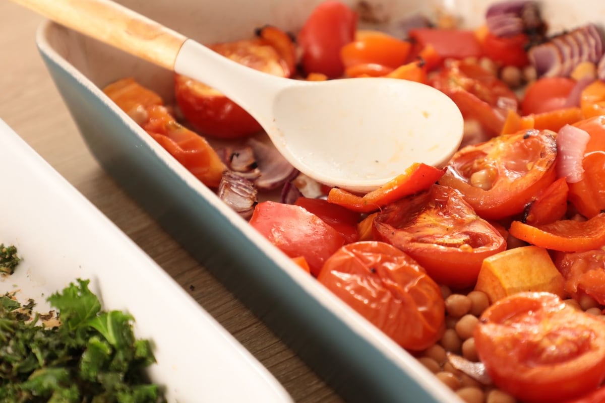 Roasted red peppers, tomatoes, chickpeas and sliced red onion in baking tray with spoon