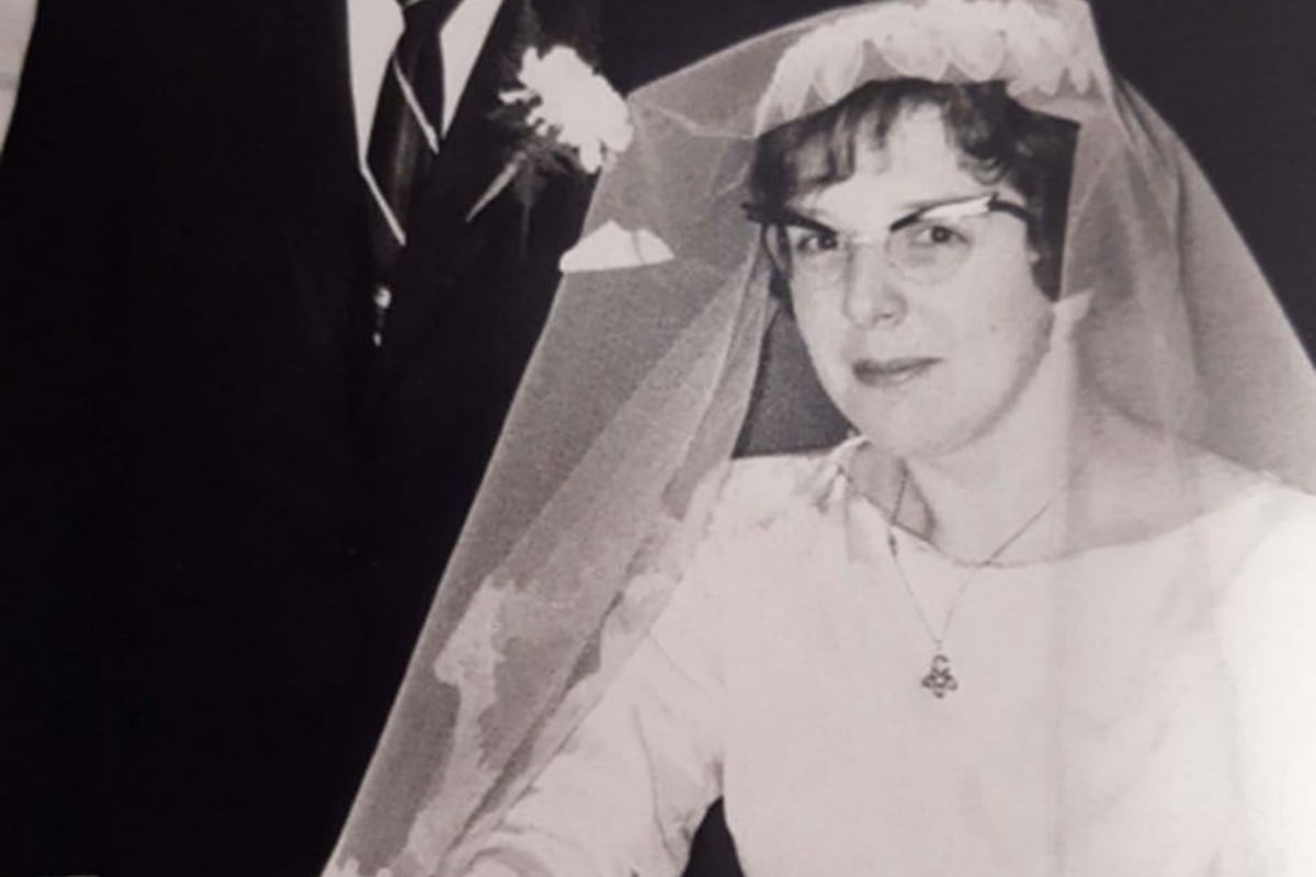 Bride in veil signing document with groom standing beside her in suit and tie