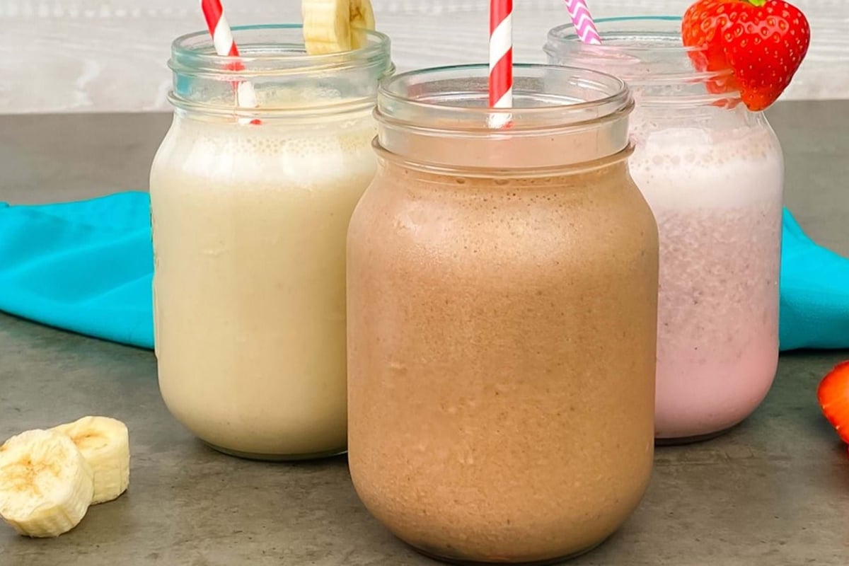 Three jars of banana, chocolate, and strawberry milkshakes with fruit garnishes and stripe