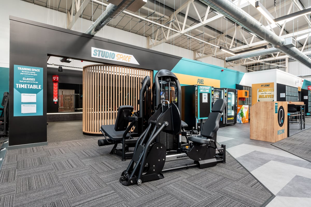PureGym Bridgend: Resistance machines, free weights, timetable signage, and rubberized studio flooring.