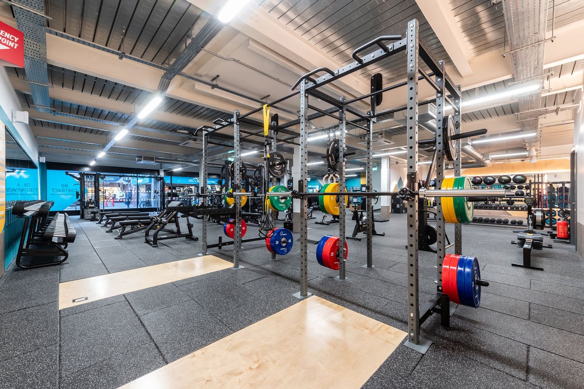 PureGym Droitwich Spa: Free weight racks, squat stands, weight plates, benches, and rubberized flooring of a gym.
