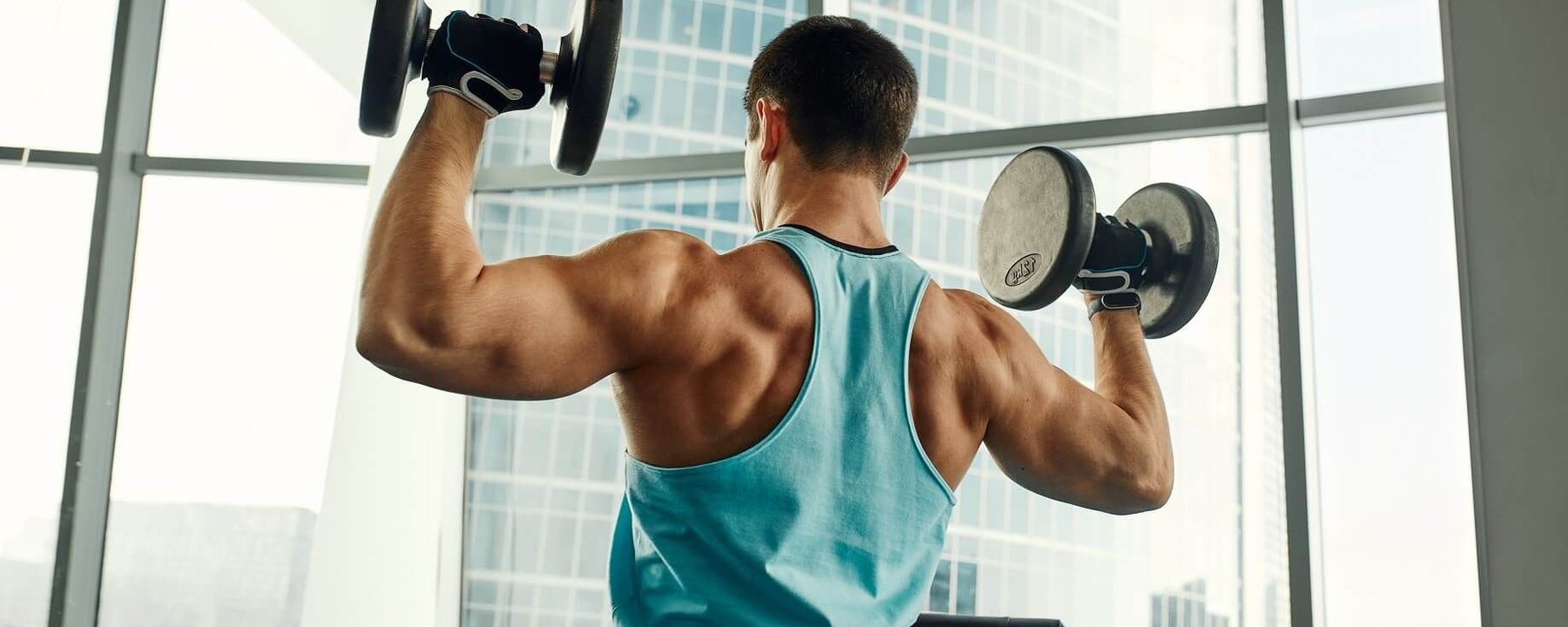 Homme soulevant des haltères dans une salle avec grandes fenêtres et vue sur la ville