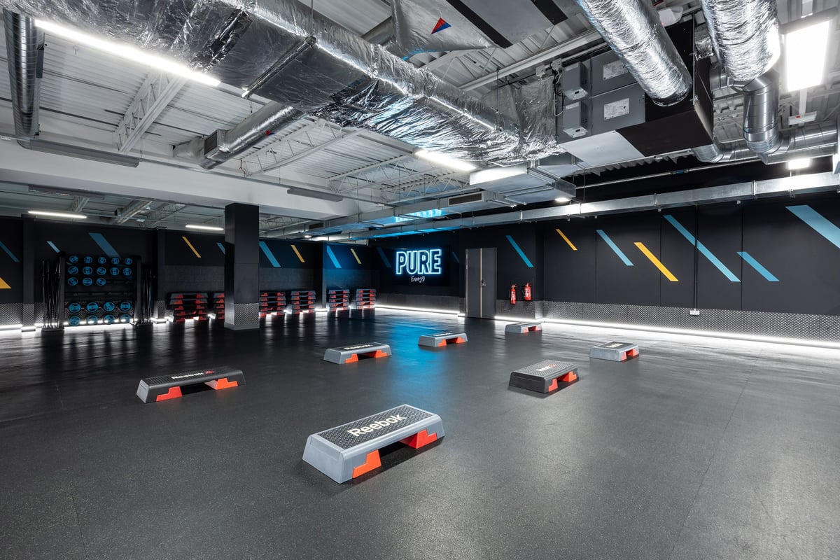 PureGym Motherwell: Black gym floor with rectangular boxes, blue neon lighting, ventilation ducts overhead.