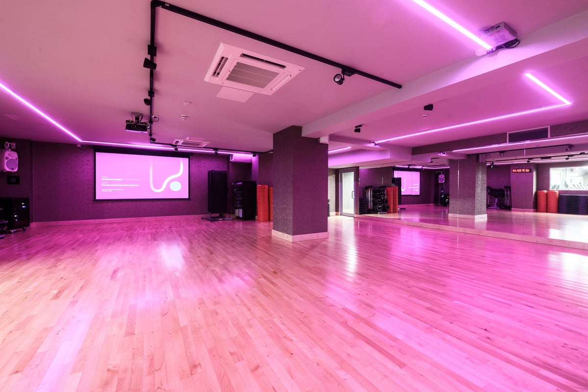 PureGym London Lewisham: Bright studio with wooden flooring, pink lighting, and projection screen.
