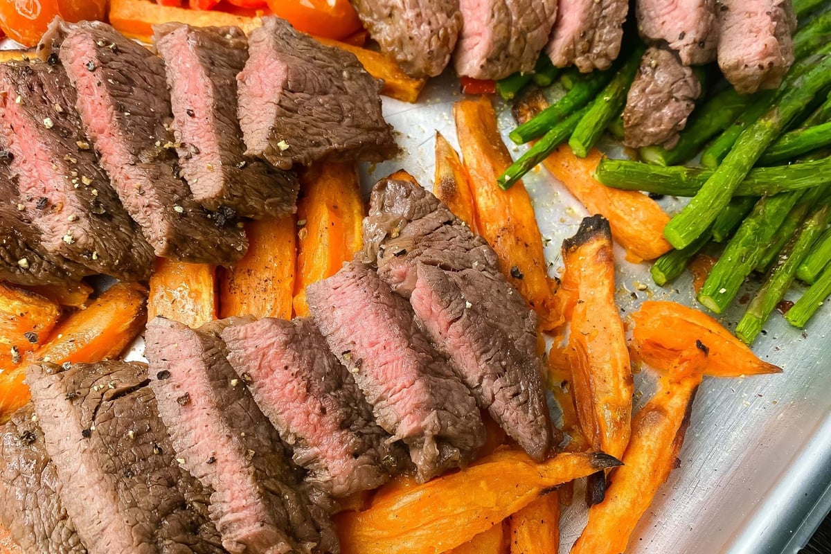 Sliced medium-rare steak with roasted carrots, asparagus, cherry tomatoes, and red peppers