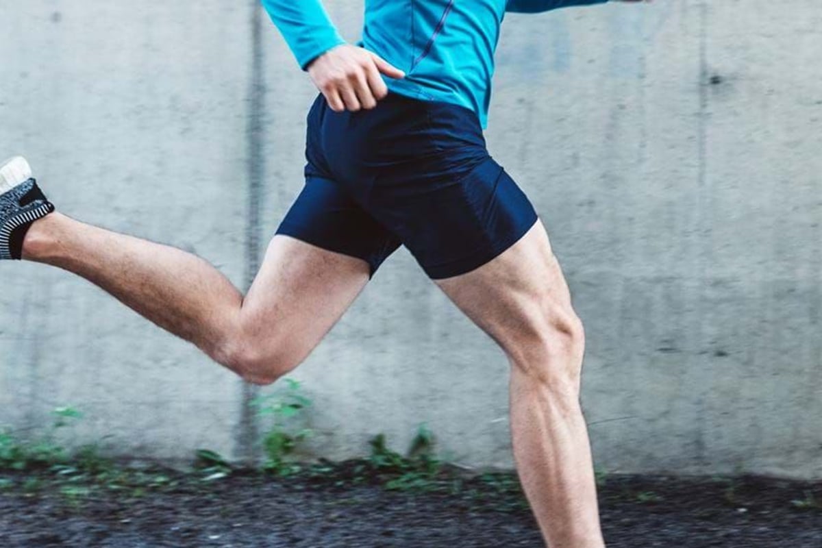 Man in blue top and black shorts running past a concrete wall outdoors