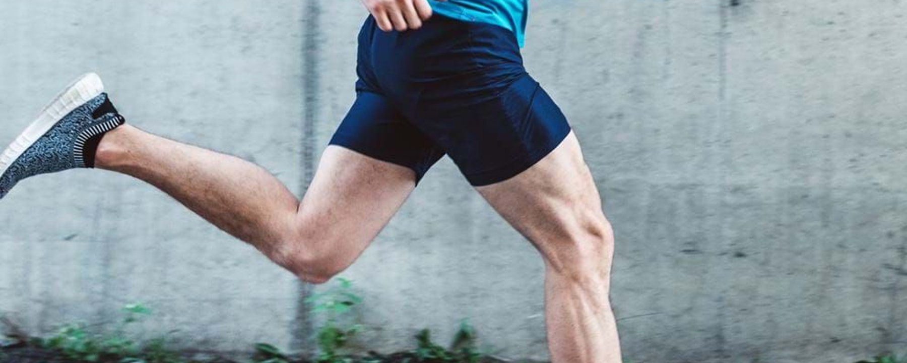 Man in blue top and black shorts running past a concrete wall outdoors