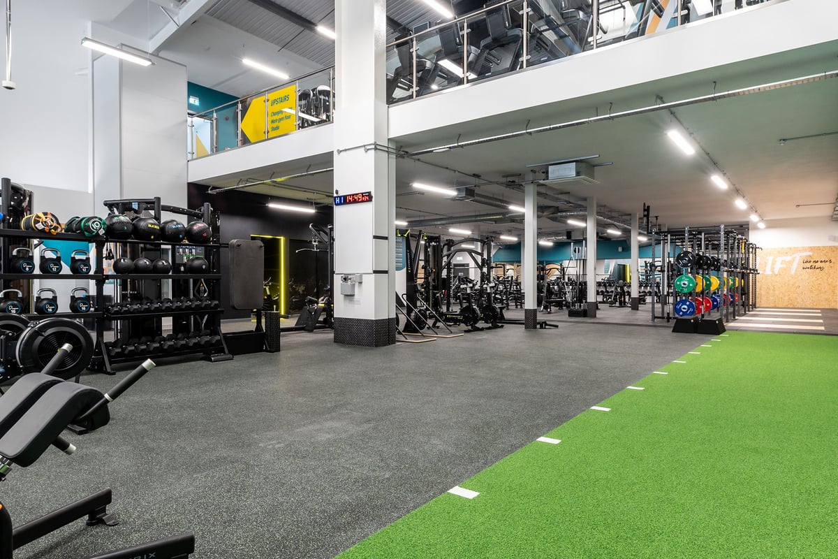 PureGym Kettering: Gym interior with weight racks, resistance machines, rubberized flooring, and colourful graffiti mural.
