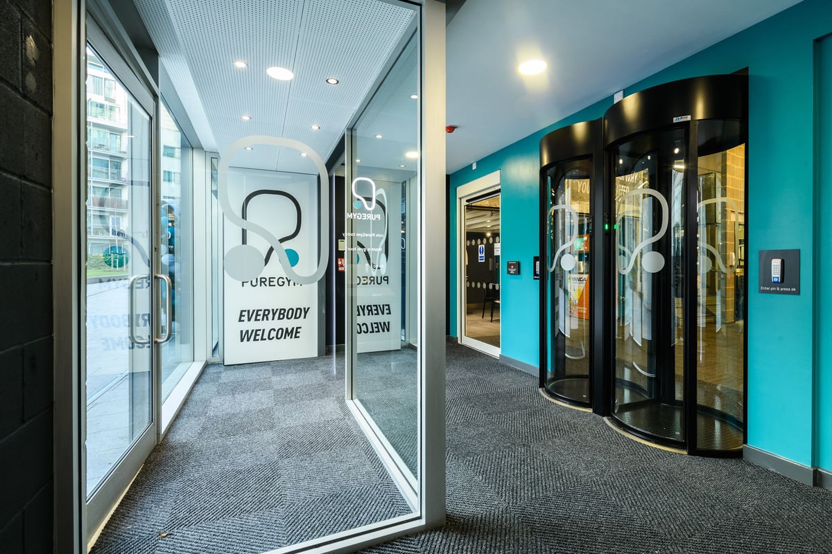 PureGym London Borough: Glass entrance doors with "Everybody Welcome" signs and teal accents.