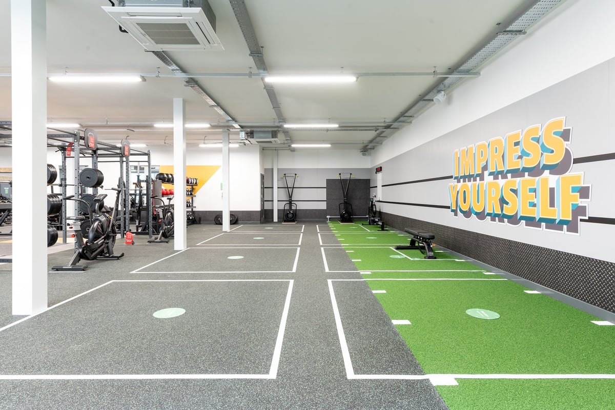 PureGym Colchester Retail Park: Squat racks, weight plates, turf area, dumbbell racks, and motivational wall graphics.