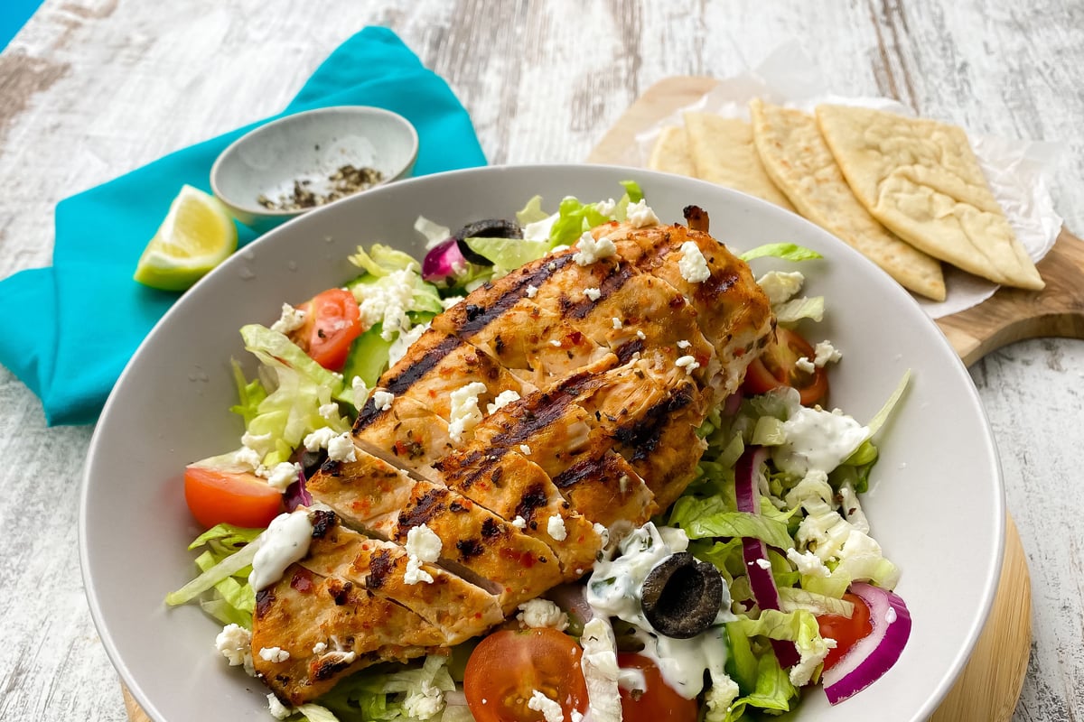 Grilled chicken slices on salad with feta, olives, tomatoes and flatbread on the side