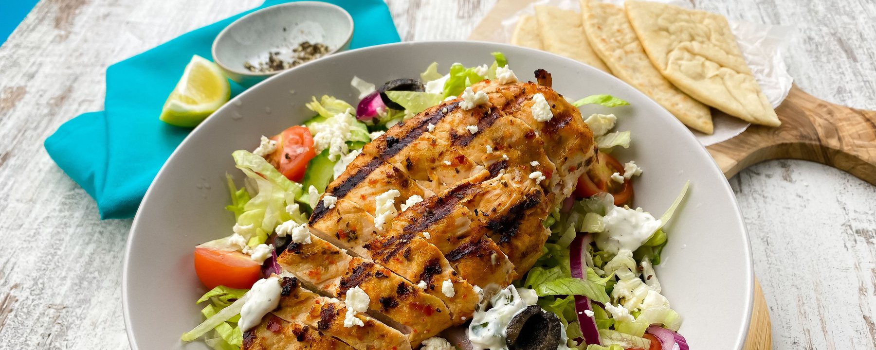 Grilled chicken slices on salad with feta, olives, tomatoes and flatbread on the side