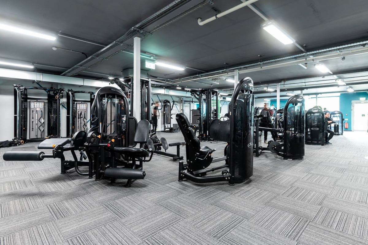 PureGym Oldham: Weight machines, resistance equipment, rubberized floor tiles in a dimly lit gym interior.