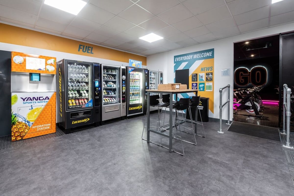 PureGym Epsom: Vending machines, seating area, and tiled flooring in what appears to be a commercial establishment.