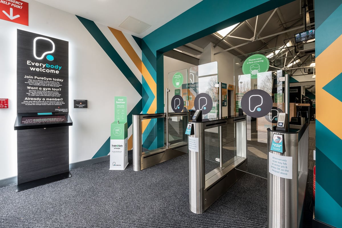 PureGym Puregym Crayford: Entrance area with turnstiles, digital signage boards, and registration kiosks.