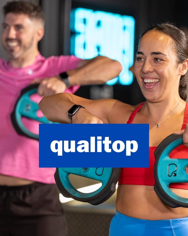 Lächelnde Frau hält Gewichte in PureGym mit Qualitop-Logo und Mann im rosa Hemd vor Neonschild-Hintergrund