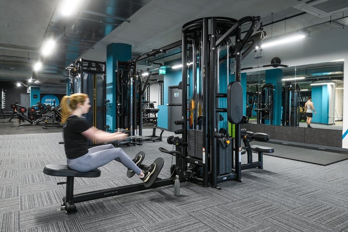PureGym Hitchin: Resistance machines, free weights, benches, and rubberized flooring in a teal and black fitness studio.