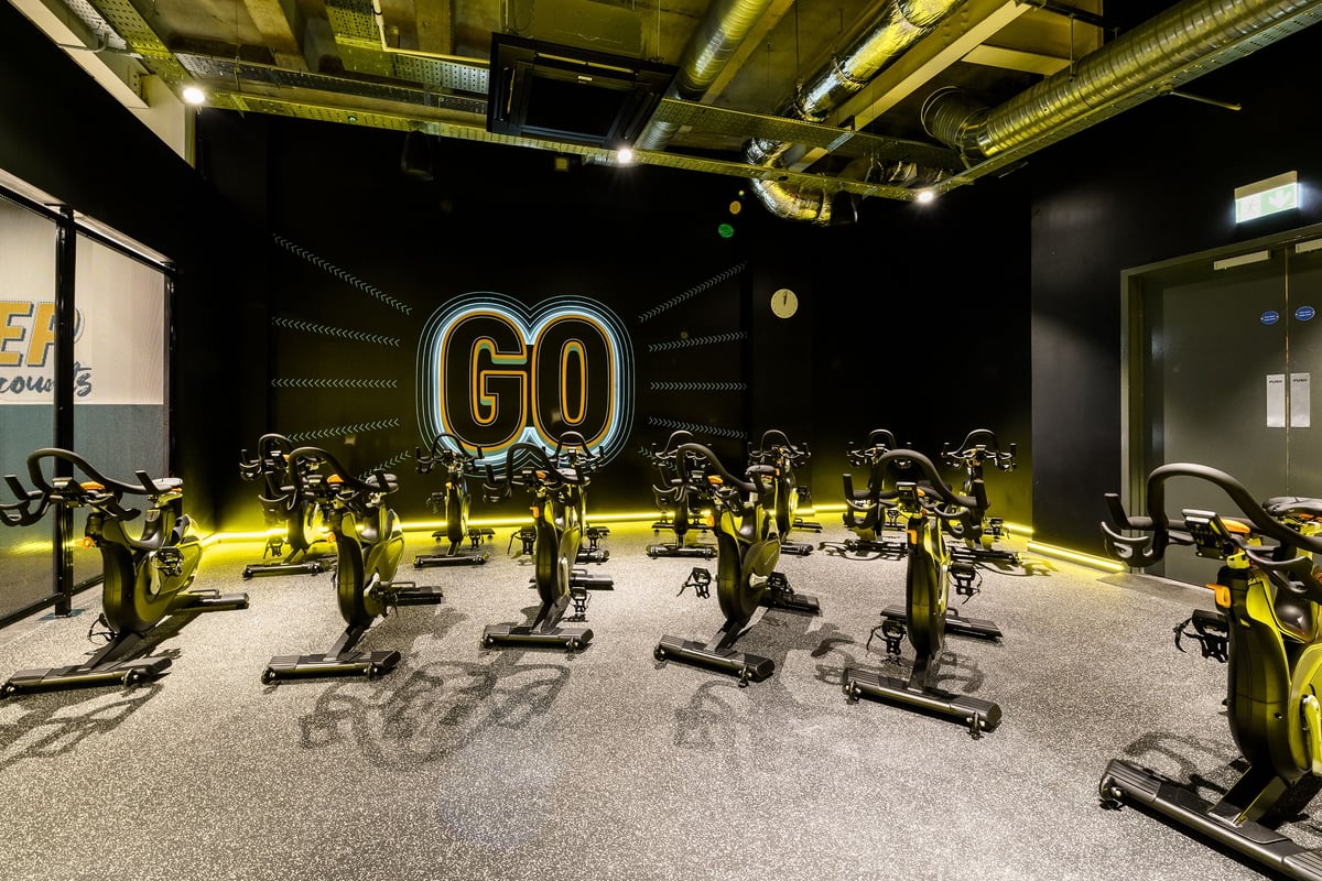PureGym London Wimbledon: Rows of stationary bikes with neon 'GO' lighting in a dimly lit studio.