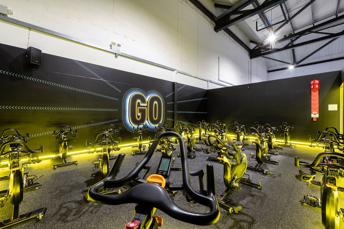 PureGym York: Rows of stationary cycling bikes, illuminated "GO" sign, and industrial-style ceiling beams.