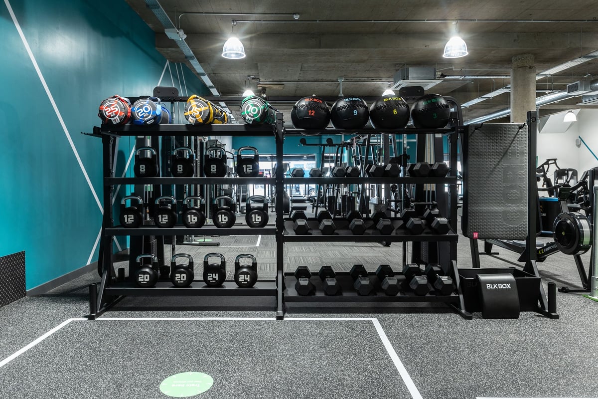 PureGym London Leytonstone: Shelves with medicine balls, kettlebells, weight plates in varied hues, rubberised floor tiles.