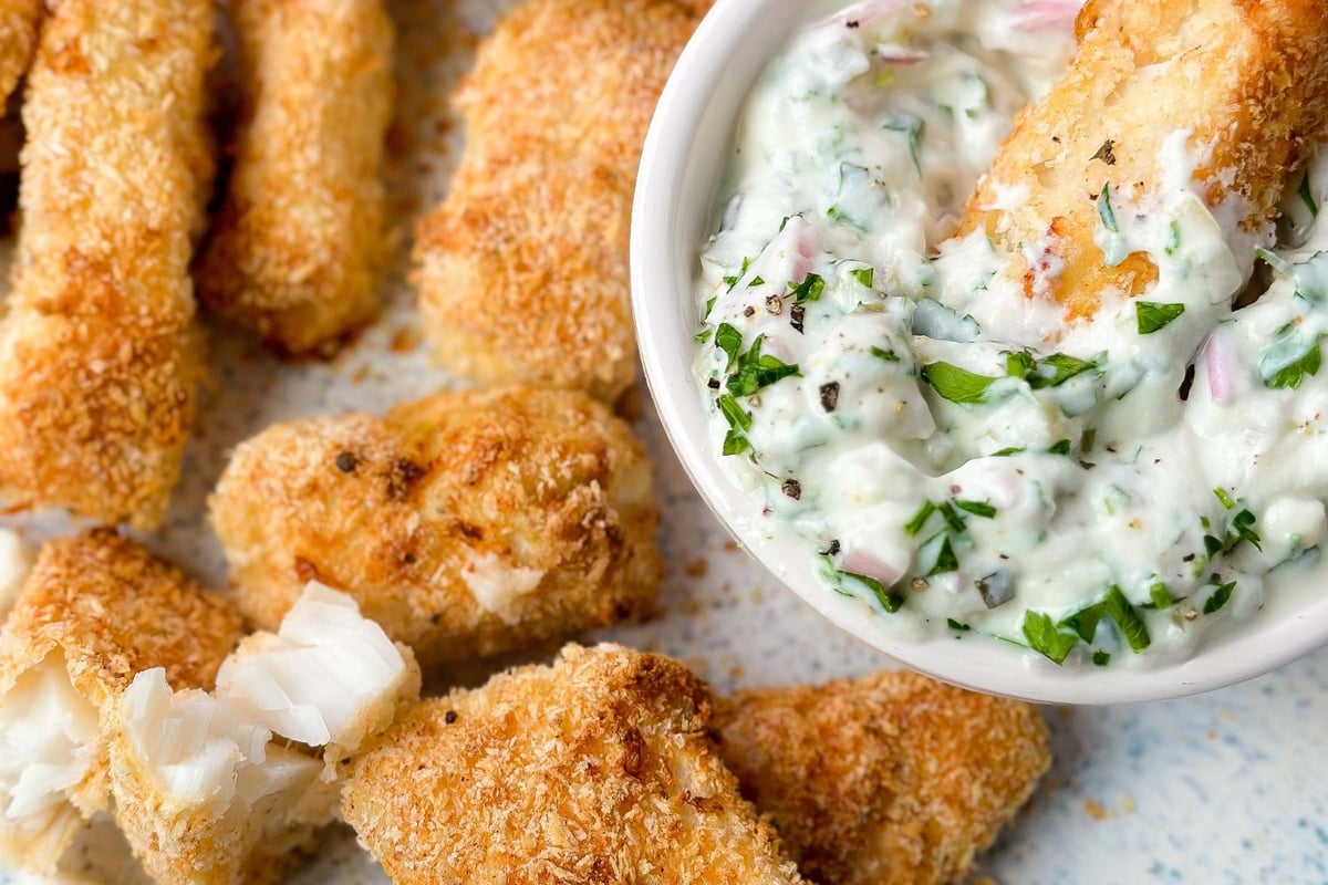 Breaded fish sticks with herb dip and lemon wedge on a speckled plate