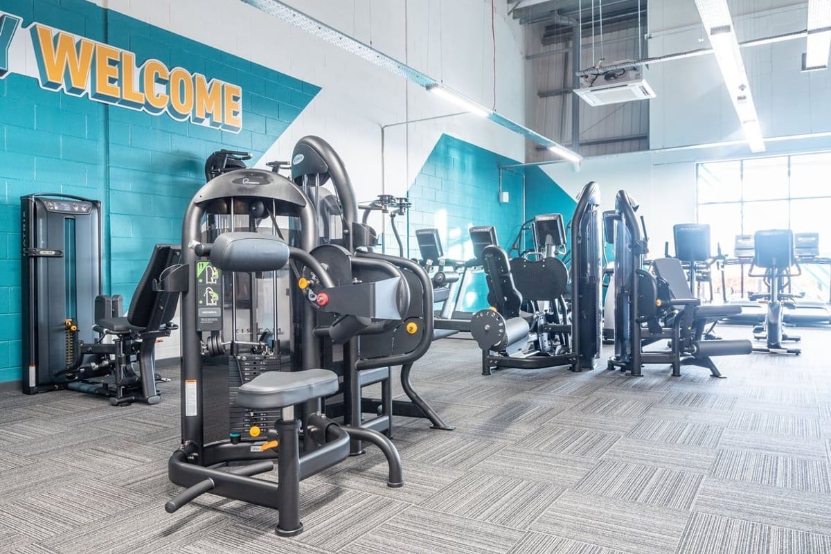 PureGym Lanark: Welcome sign, strength machines, weight benches, rubberized flooring in a gym or fitness studio interior.