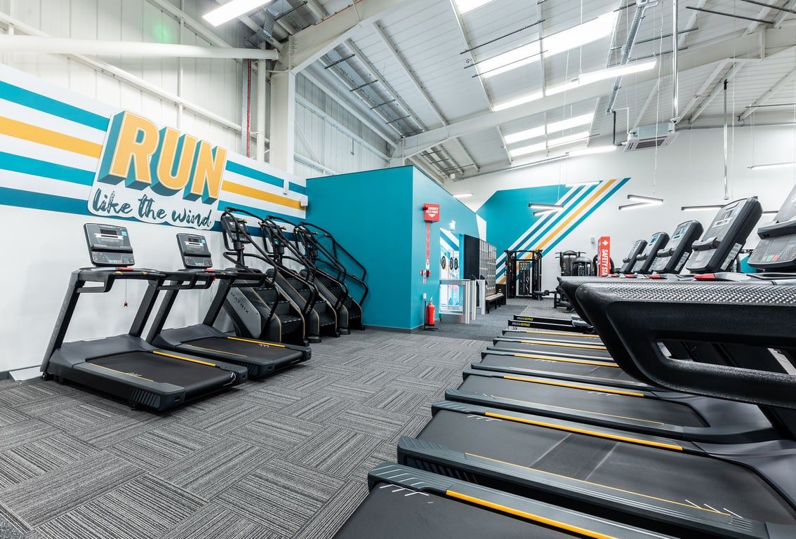 PureGym Eastbourne: Rows of treadmills, large motivational wall signage, and rubber flooring - a typical cardio area.