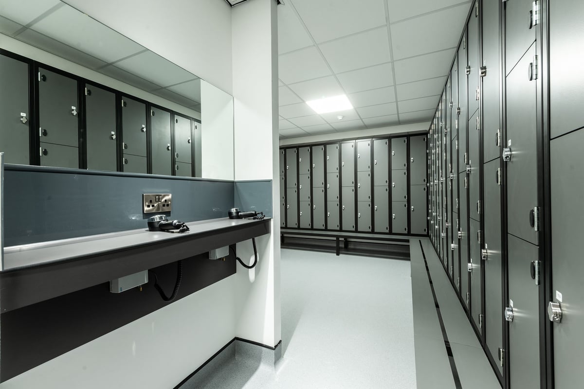 PureGym Macclesfield Silk Road: Rows of lockers, benches, in a gray utilitarian changing room setting.