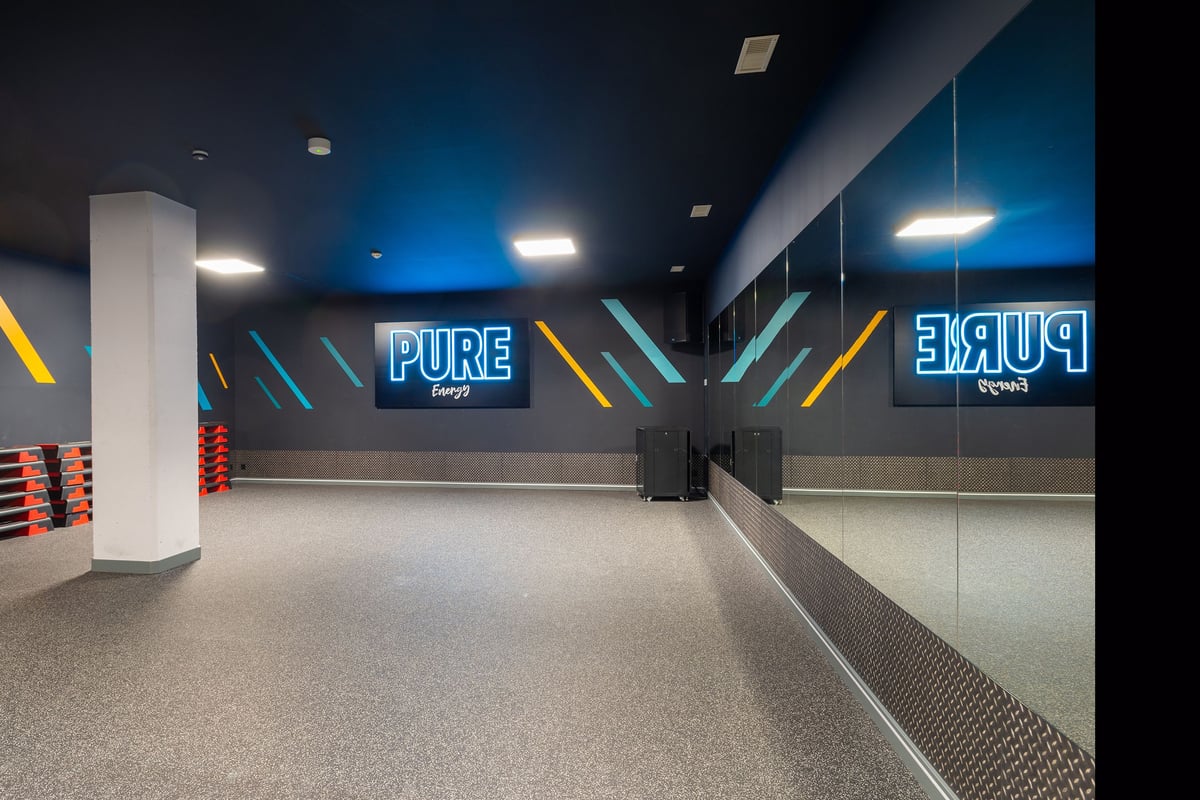 PureGym La Chaux-de-fonds: Hallway with blue lighting, mirrored walls, rubberized flooring, and Pure gym branding visible.