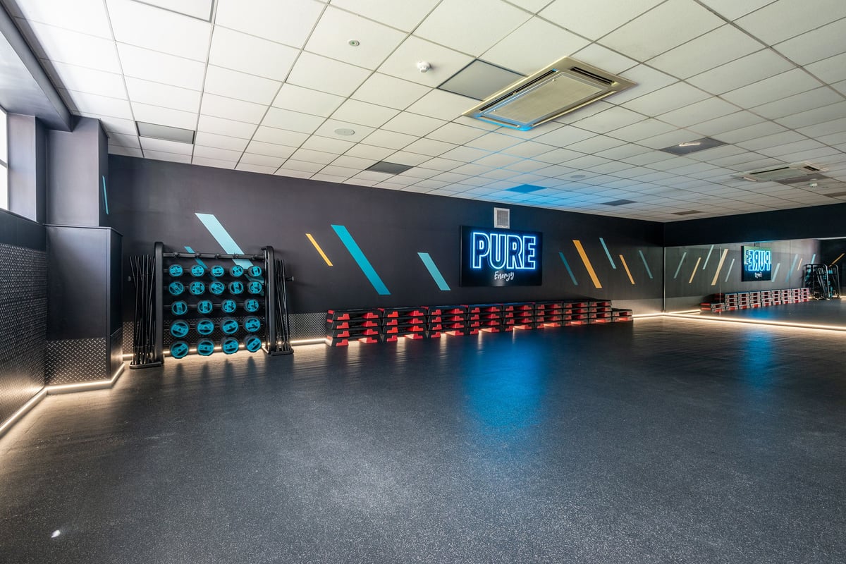 PureGym Northwich: Rows of studio cycling bikes with neon lighting, mirrored wall and sound system.