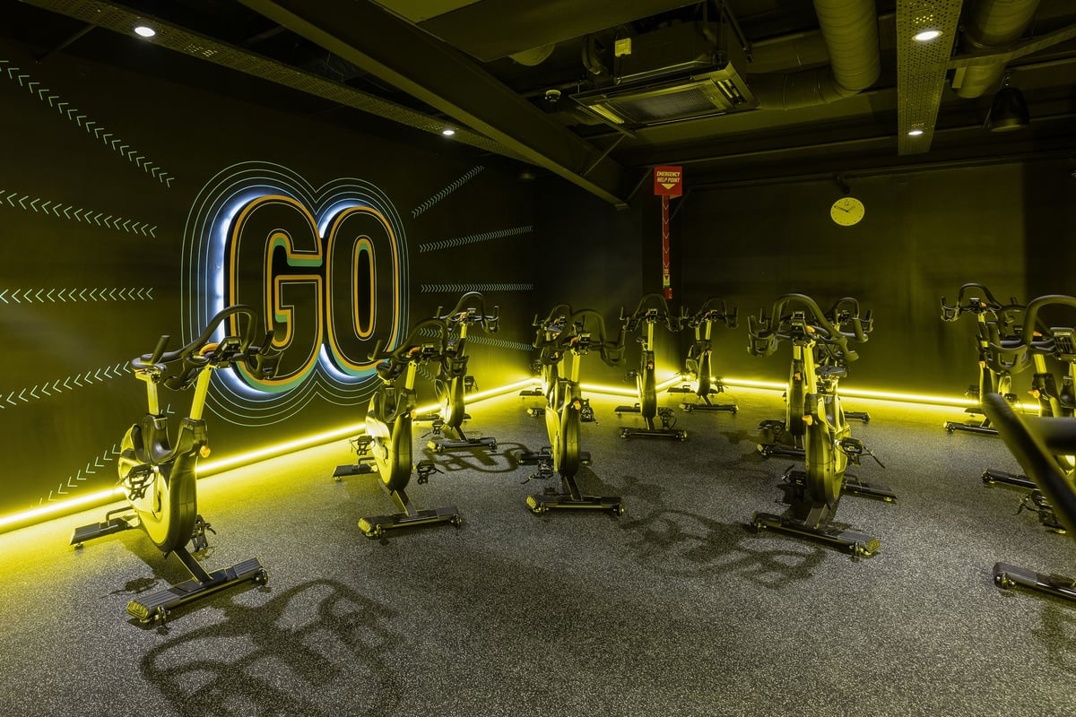 PureGym Falkirk: Rows of stationary bikes, neon 'GO' sign, yellow accent lighting in a dimly lit studio.