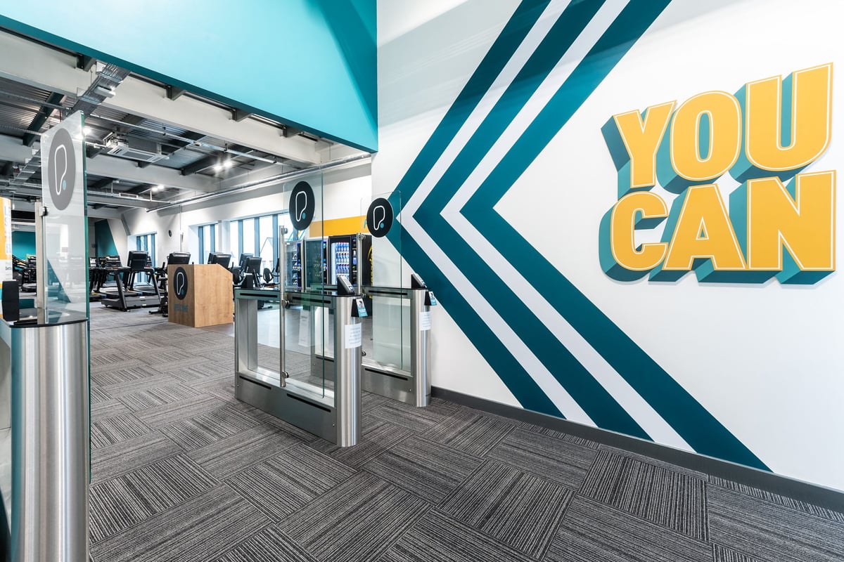 PureGym Bicester: Turnstiles, closed kiosks, "You Can" motivational signage in a modern gym setting.