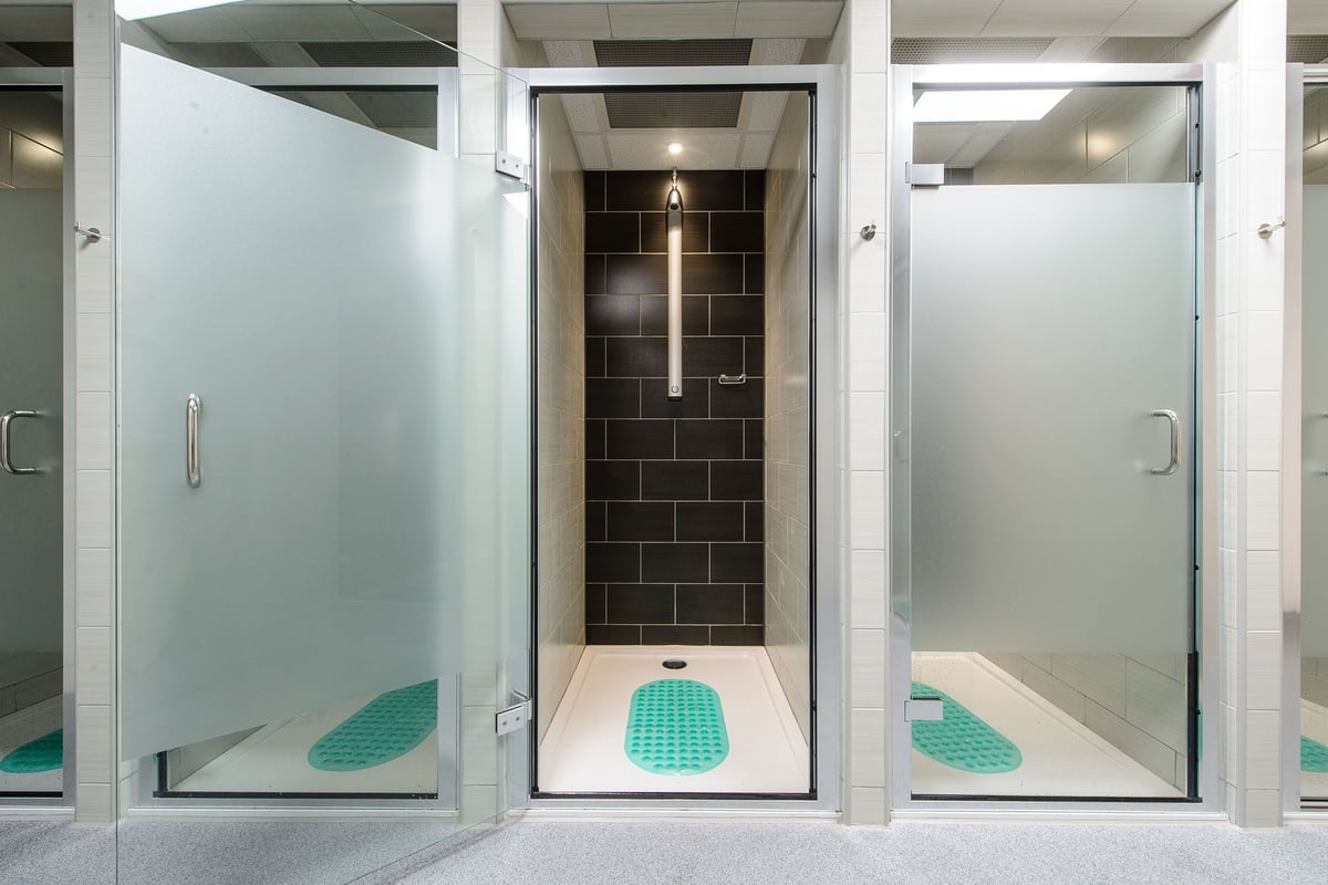 PureGym Denton: Shower facilities with tile walls, frosted glass doors, and aqua footbaths.